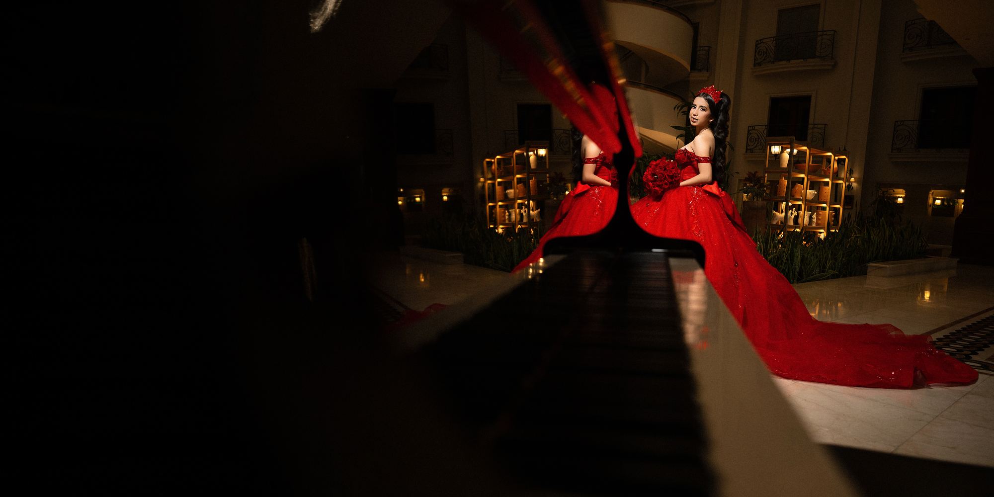 Quinceañera con vestido rojo reflejada en un piano en un salón con luces