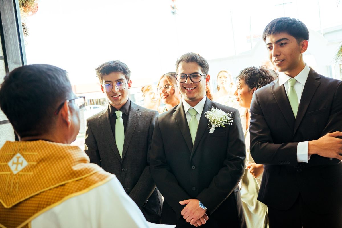 Novio y padrinos sonriendo con el sacerdote en la entrada de la iglesia