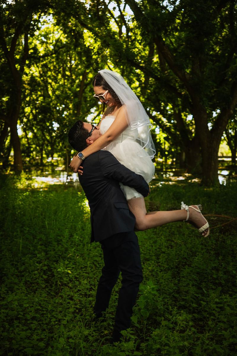 Novio cargando a la novia entre árboles