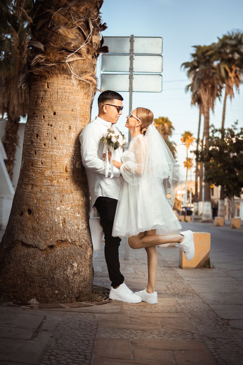 Novios junto a una palmera, ella con vestido corto y velo