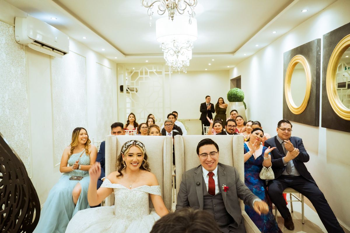 Novios sentados sonriendo mientras su familia aplaude
