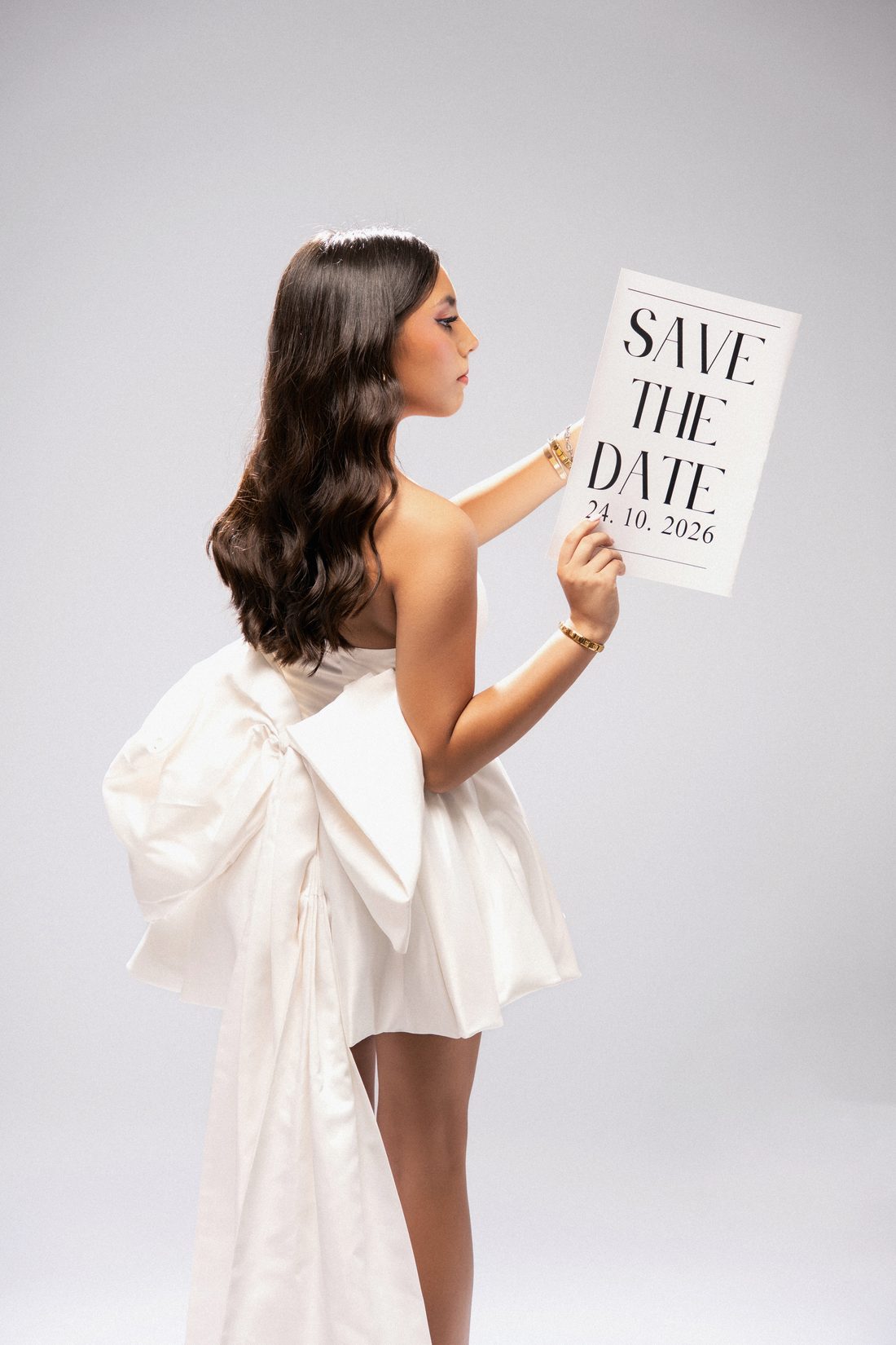 Joven con vestido blanco de moño sosteniendo un letrero de save the date