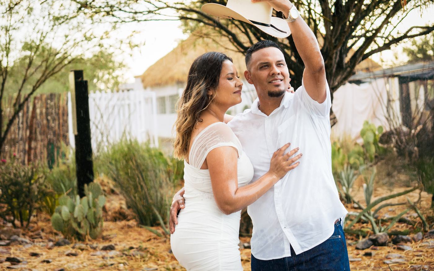 Pareja sonriendo en un jardín, él levanta su sombrero