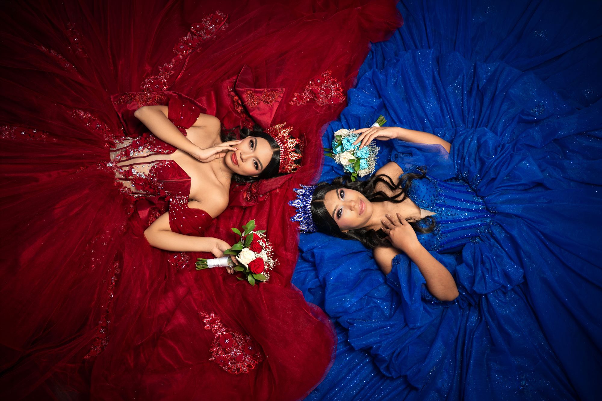 Dos quinceañeras recostadas con vestidos rojo y azul