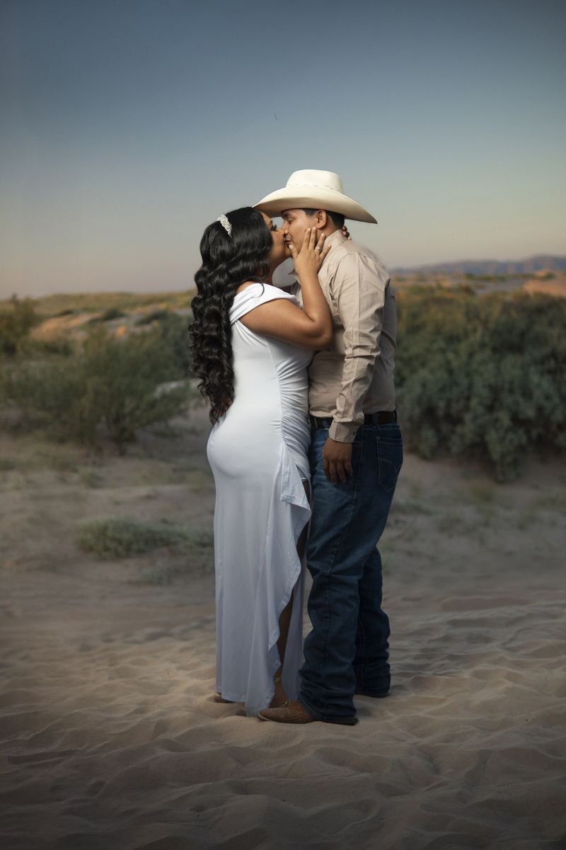 Pareja besándose en las dunas, él con sombrero