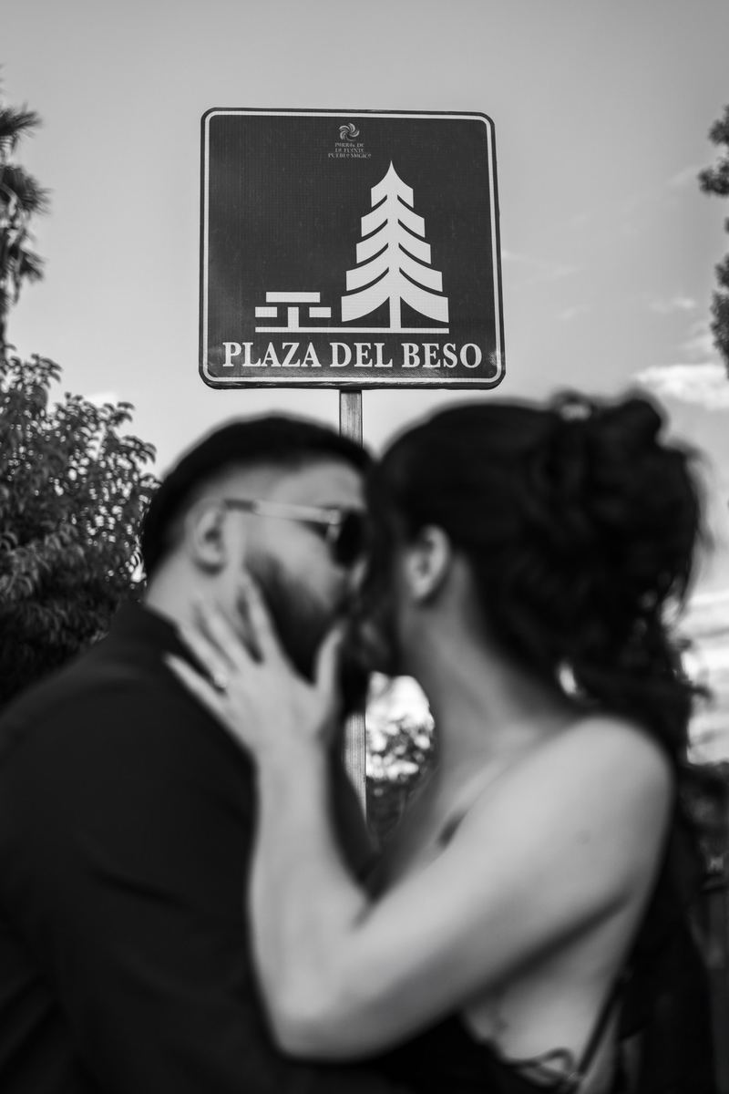 Pareja besándose bajo el letrero de la Plaza del Beso, en blanco y negro