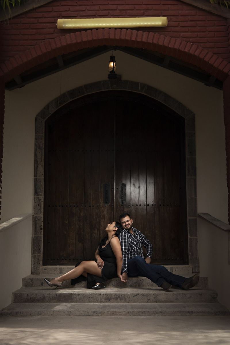 Pareja sentada espalda con espalda frente a un portón de madera