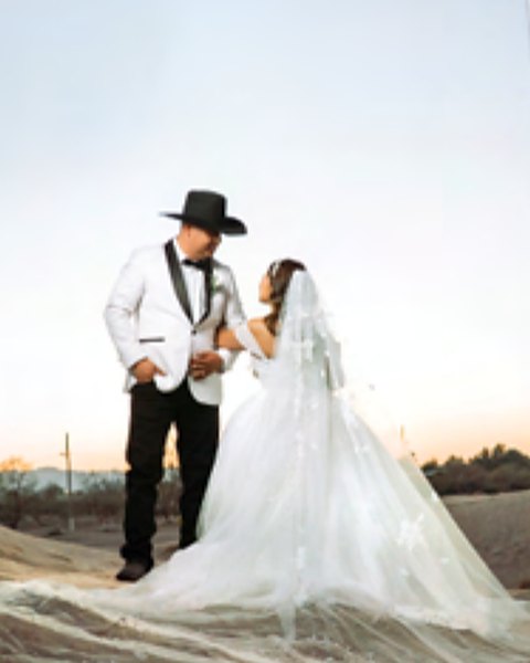 Karen con vestido de novia y Cesar con sombrero sobre las dunas al atardecer