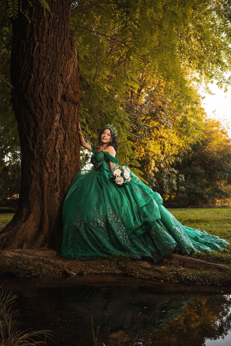 Quinceañera con vestido verde bajo los árboles con luz de tarde