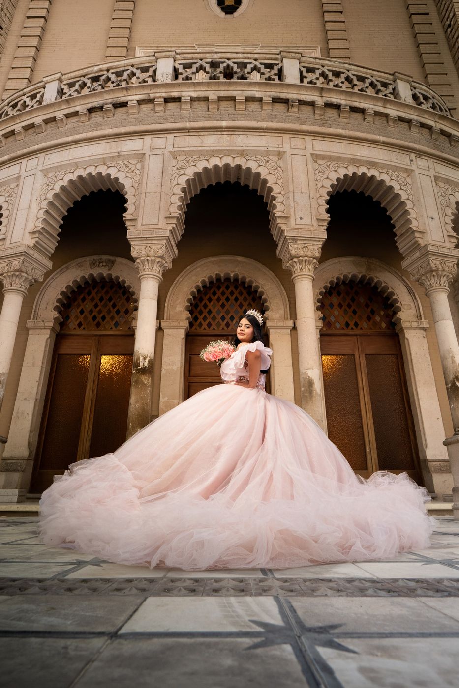 Quinceañera con vestido rosa frente a unos arcos