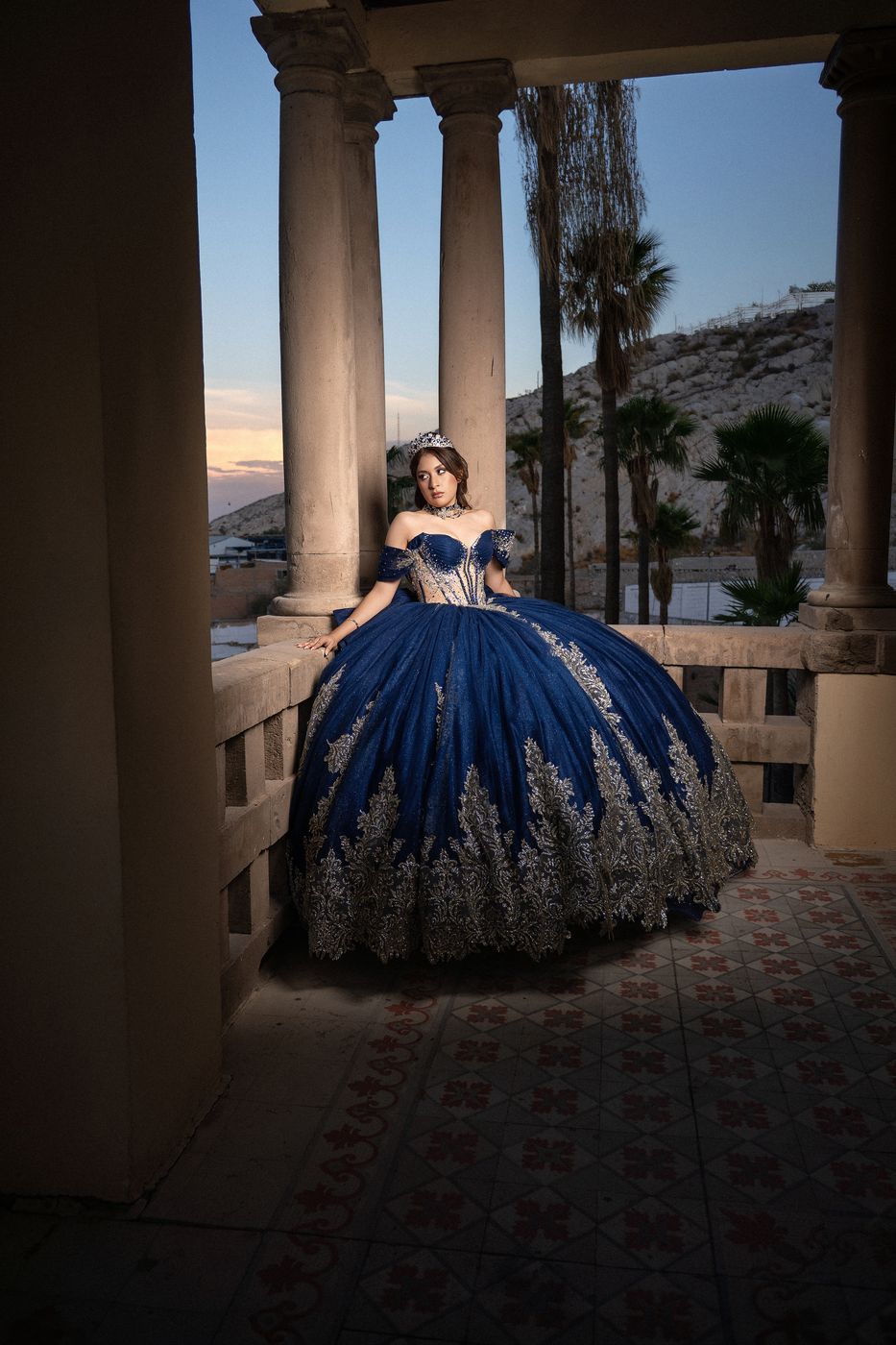 Quinceañera con vestido azul marino en un balcón al atardecer